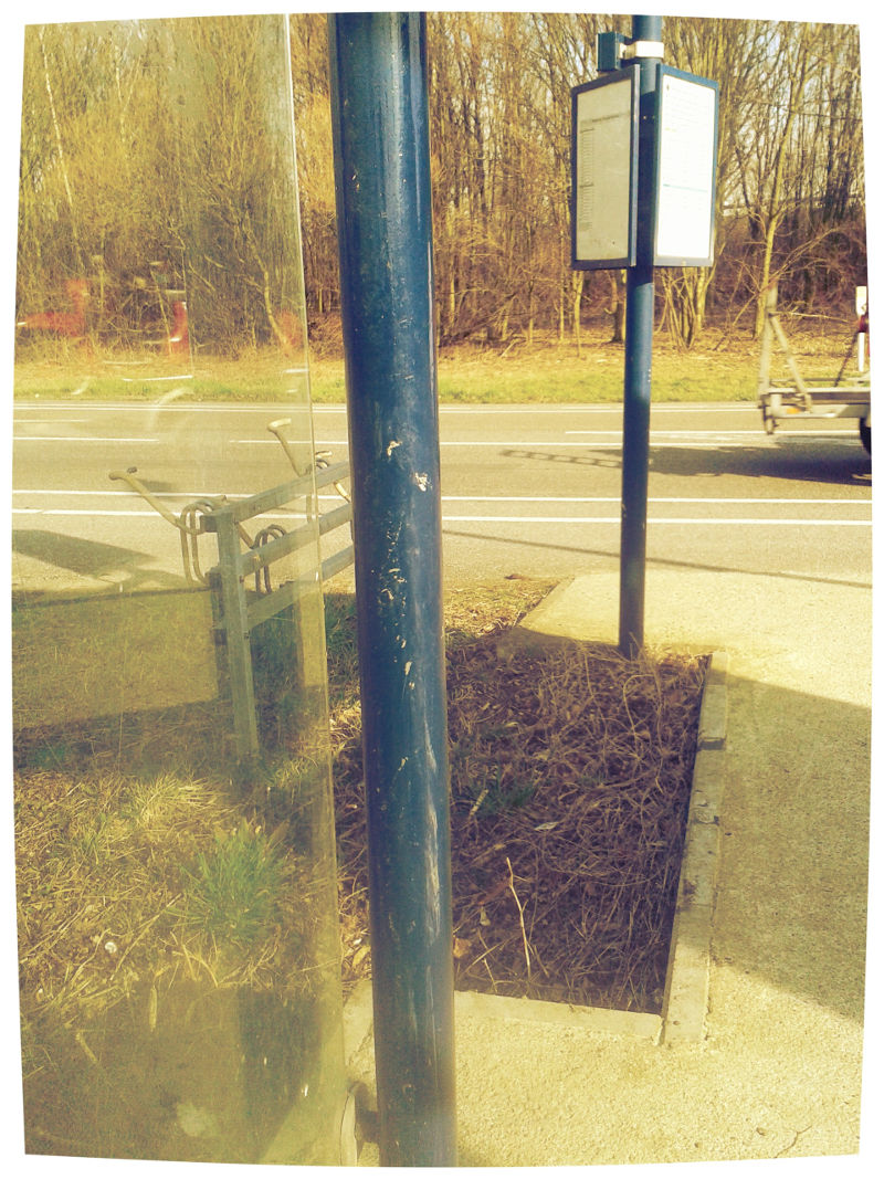 Blick von der Bank der Bushaltestelle im Nirgendwo vorbei am Haltestellenschild auf die befahrene Stra�e.