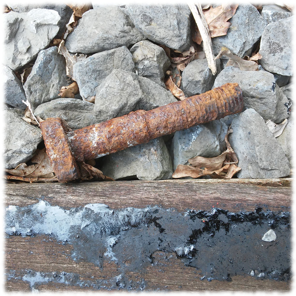 Gro�e rostige Schraube zwischen Schotter und Schwelle eines Gleises.