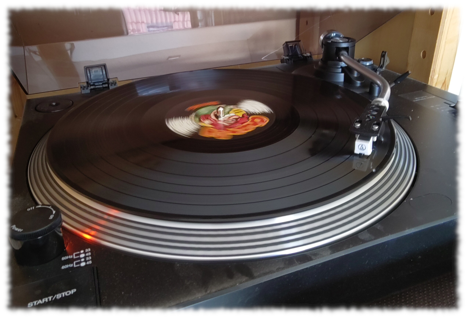 Klassischer Schallplattenspieler mit darauf rotierender Schallplatte, Abtastnadel im Bereich des zweiten Titels